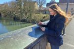 Frau blickt auf Tablet, Stift in der Hand, sonniger Wind weht durch ihre Haare.