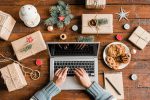 Schreibtisch mit Laptop von oben, umgeben von weihnachtlichen Geschenken und Gebäck.