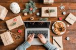 Schreibtisch mit Laptop von oben, umgeben von weihnachtlichen Geschenken und Gebäck.