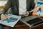 Mann hält Tablet in einer Hand, Stift zeigt auf Diagramme und Statistiken.